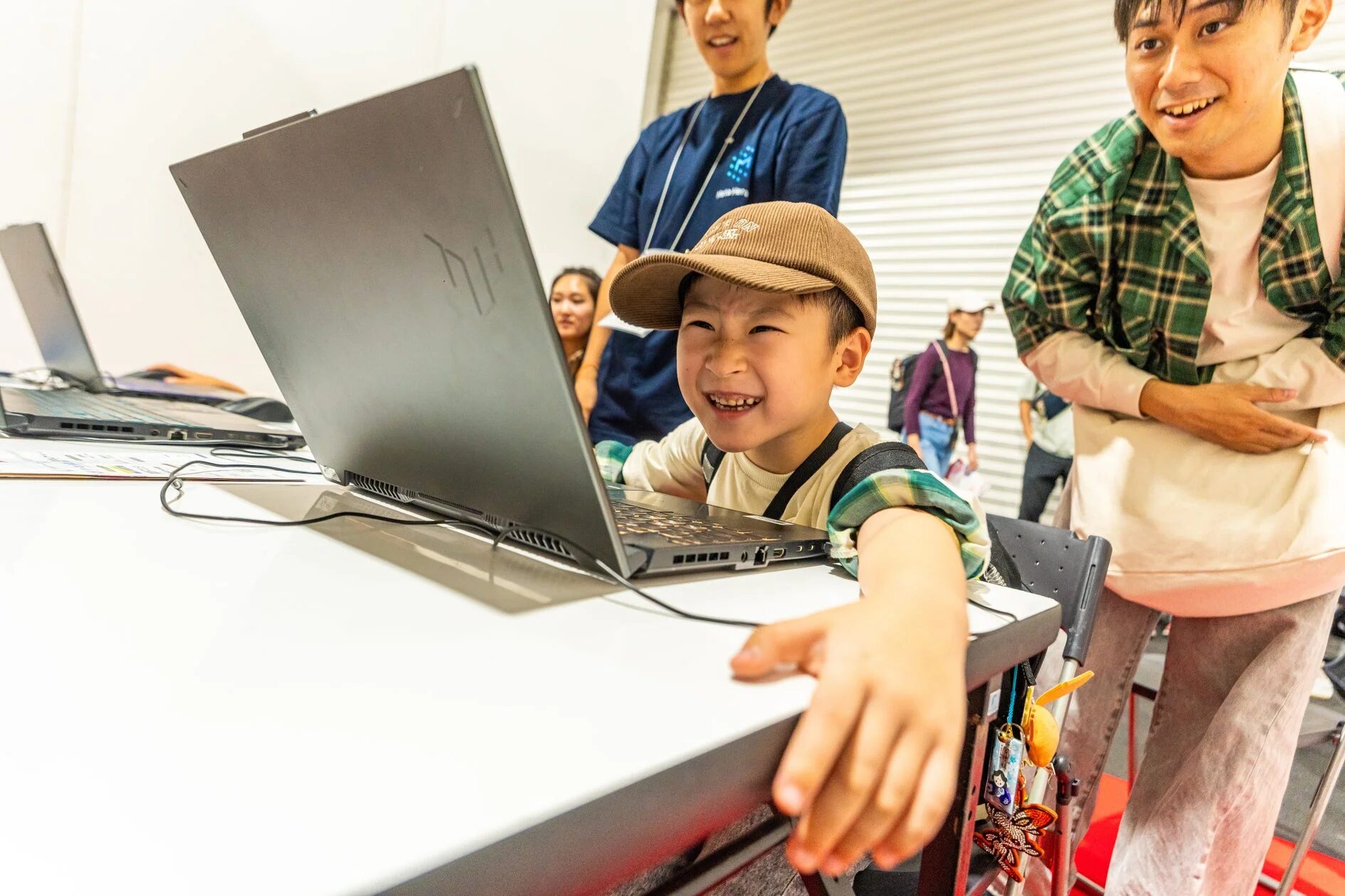 子供がノートPCを操作し、大人たちが見守る様子