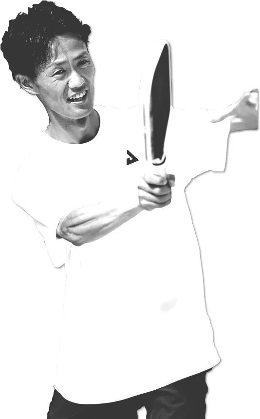 白いTシャツを着た吉原哲平選手がラケットのようなものを持ち笑顔を見せている白黒写真