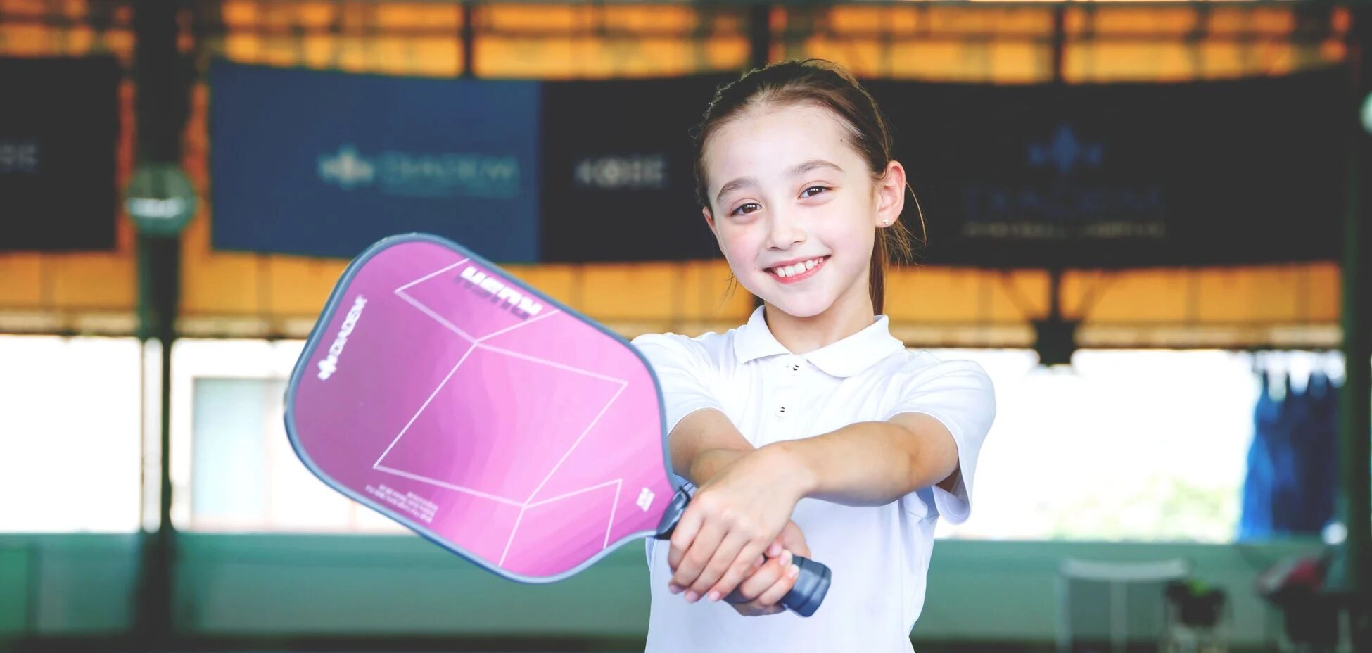 白いポロシャツを着た少女が紫色のピックルボール用パドルを持って笑顔で写っている画像