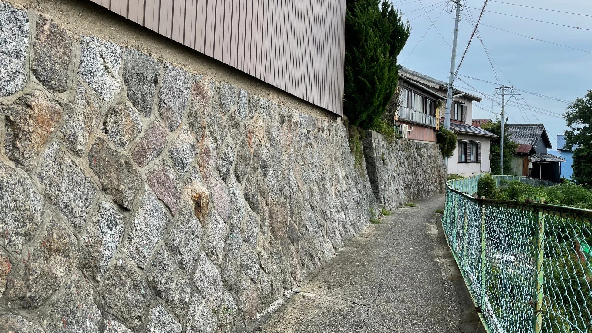 石垣とフェンスに挟まれた細いコンクリートの道