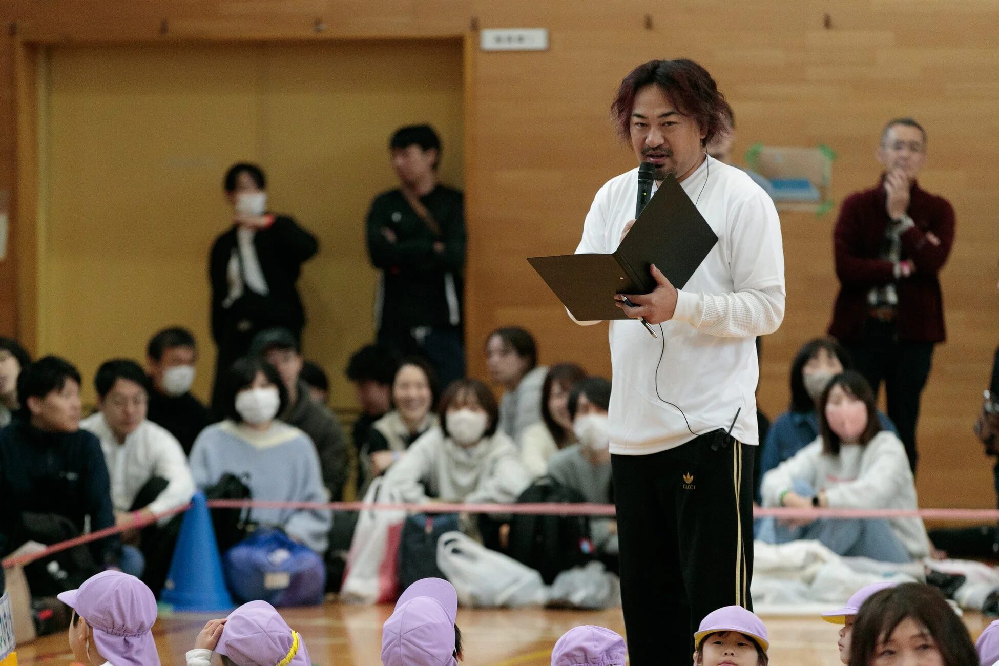 体育館でスピーチをする男性と見守る子どもたち