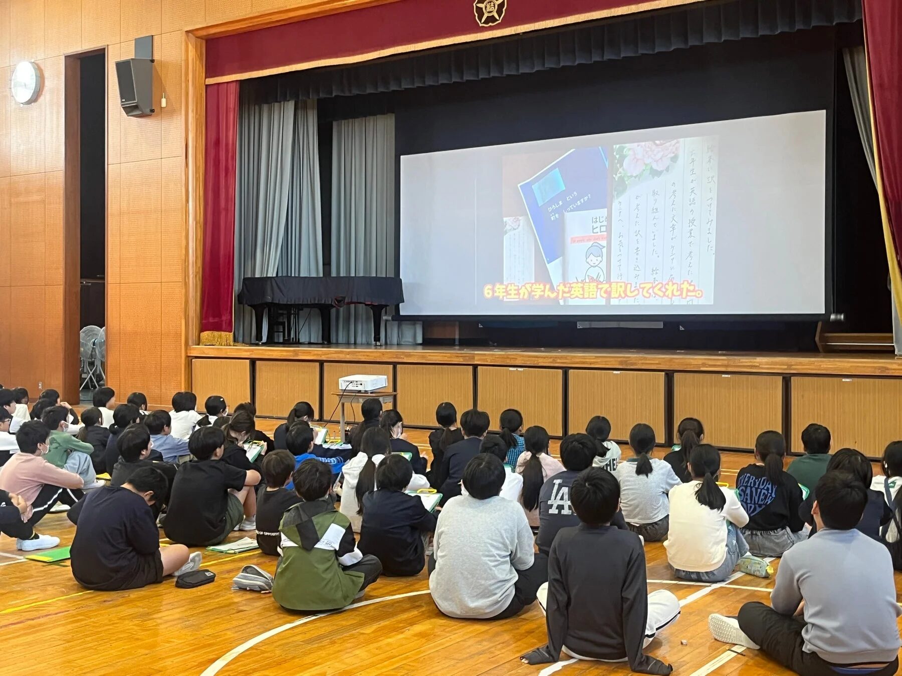 体育館でプレゼンテーションを見る小学生たち