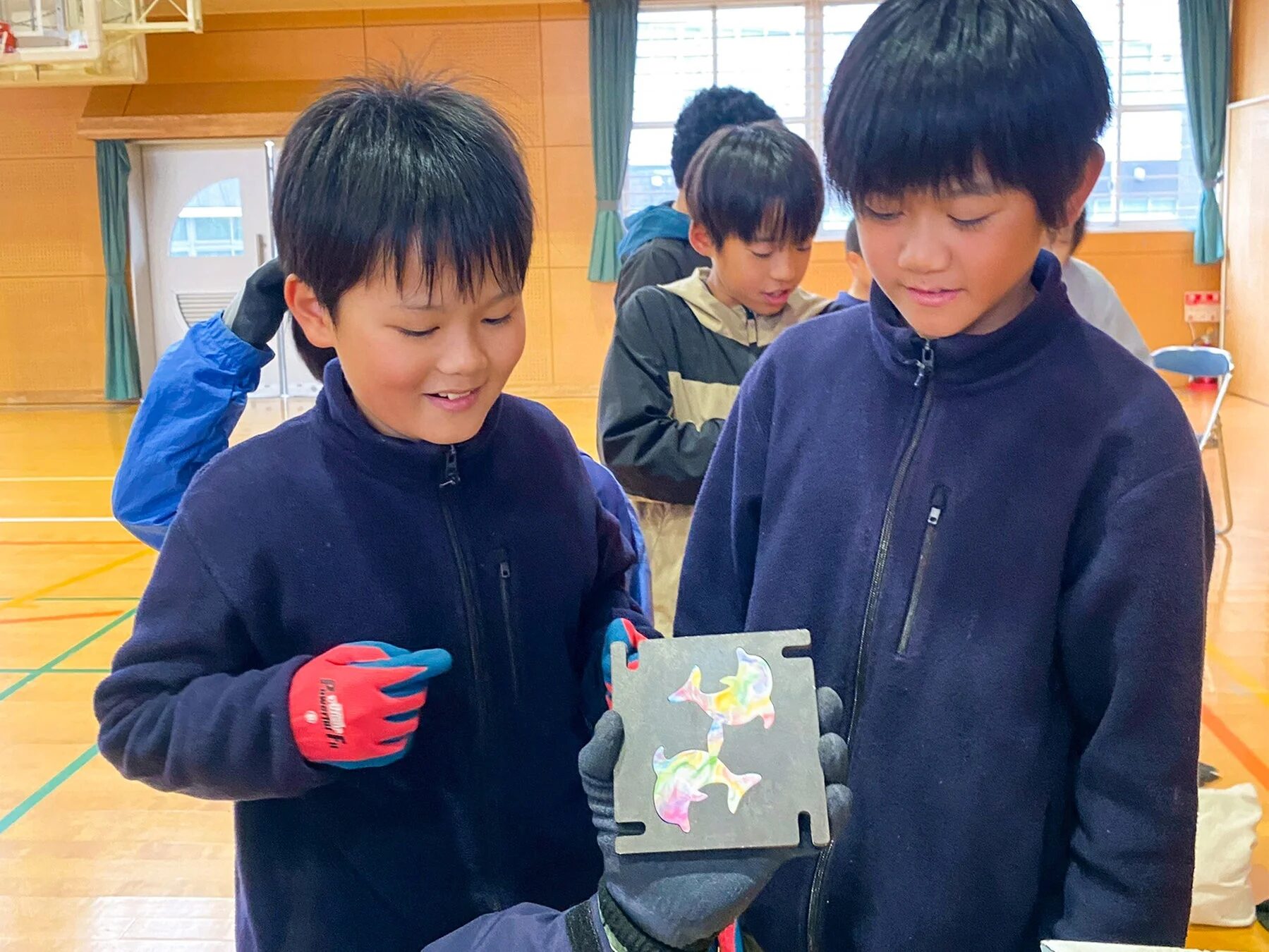 体育館で、二人の男の子がカラフルなイルカのデザインが施された金属板を興味深そうに見ています。