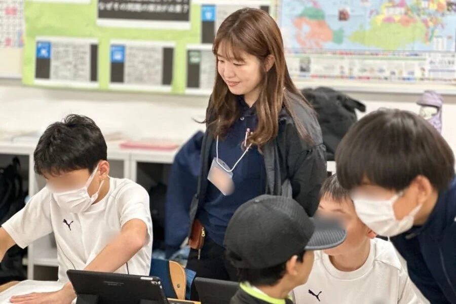 世界地図のある教室で生徒と話す先生