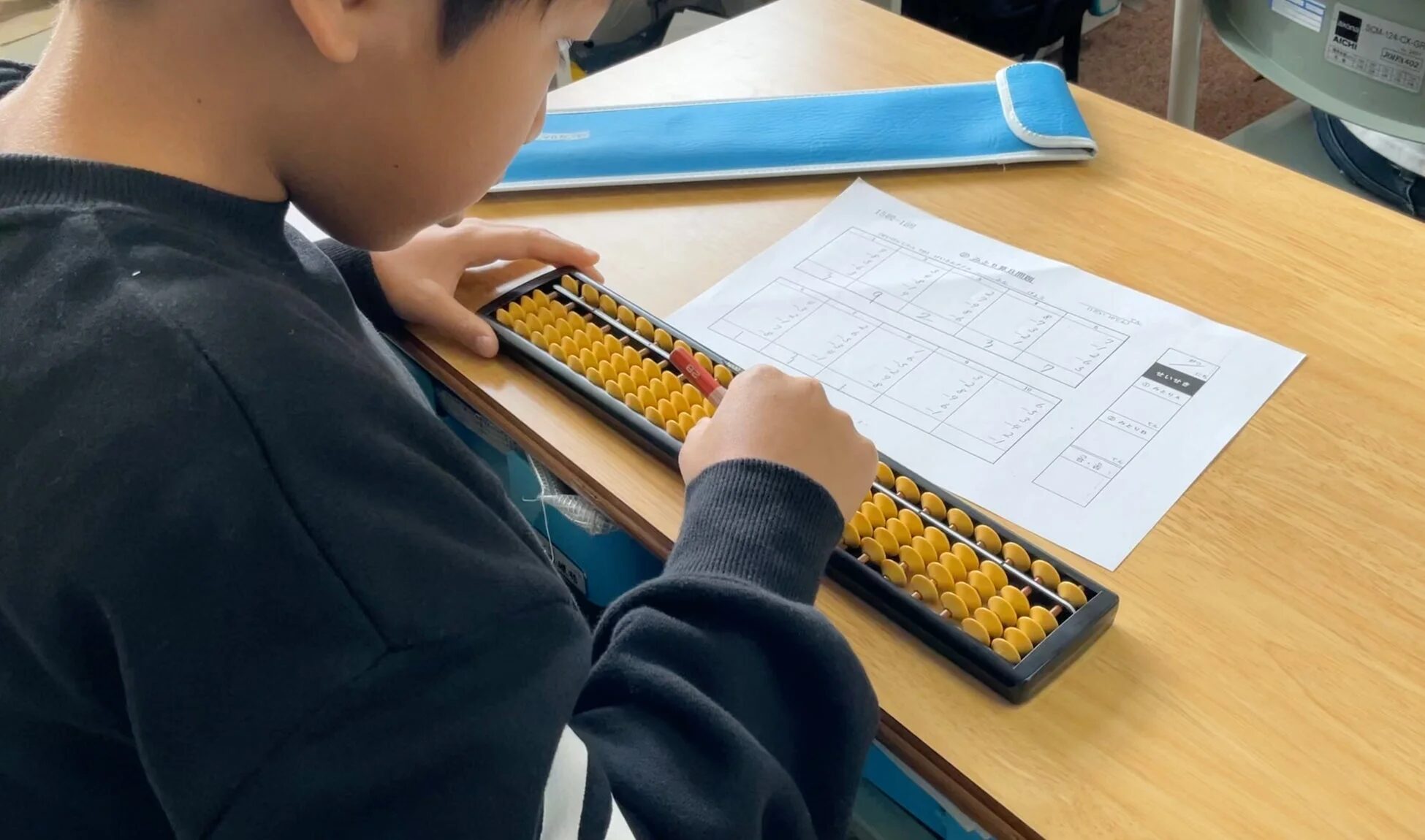 机に向かいそろばんを使って計算練習をする子供