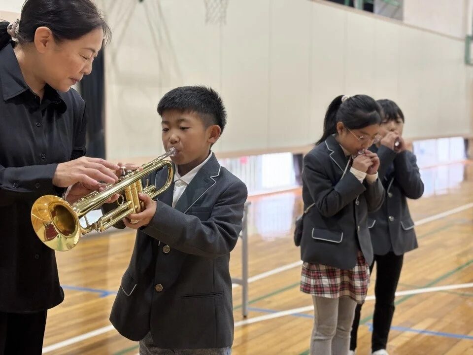 体育館でトランペットの吹き方を指導する先生と生徒
