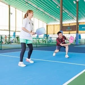 青いインドアコートで、男女2人がラケットスポーツを楽しんでいる様子