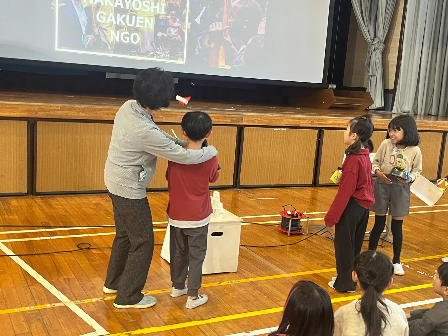 児童と大人がスクリーンを見る様子