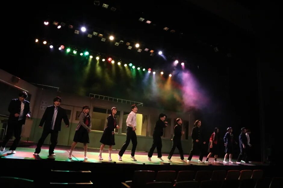 舞台上で演技やダンスをする学生服のパフォーマーたち