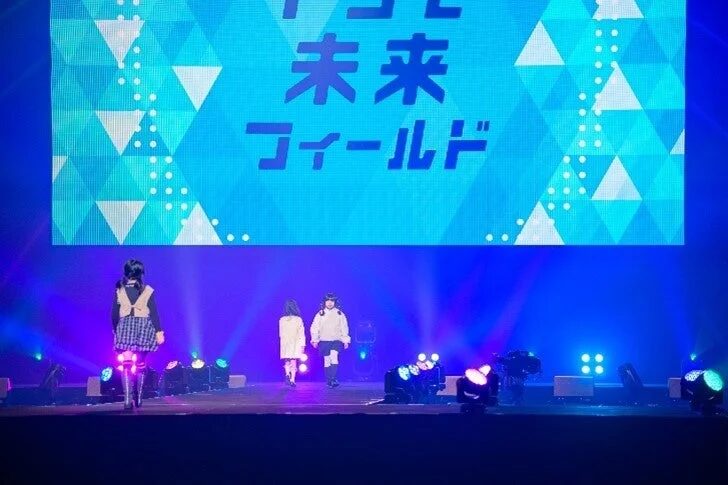 青い照明が照らすステージで、数名の人々が歩いています