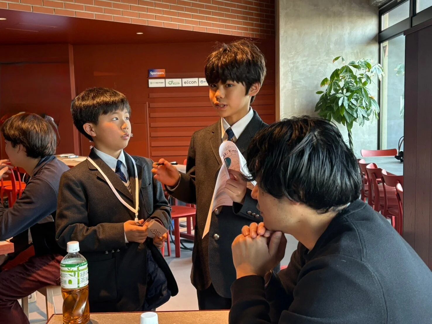 子供と大人が話している様子、スポンサーロゴあり