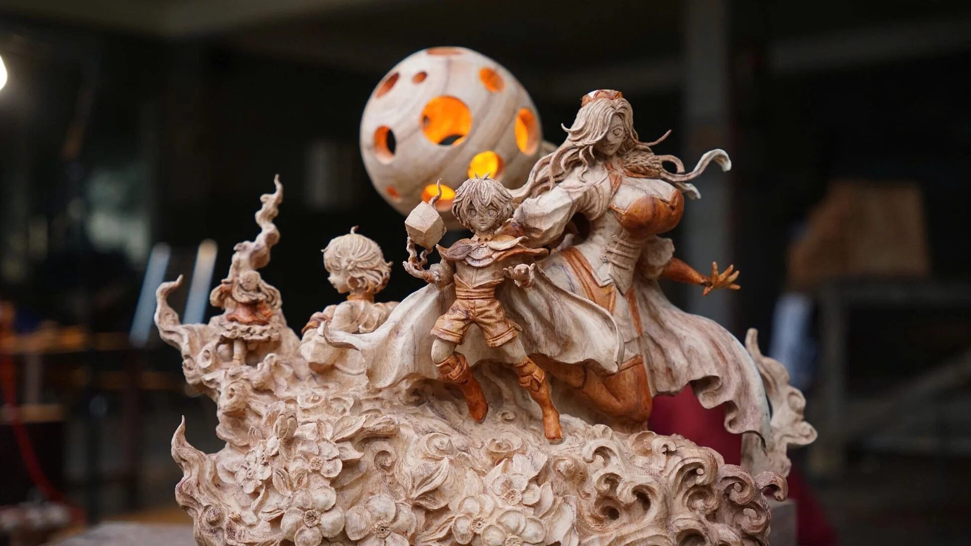 複数のキャラクターと幻想的な月が配置された、精巧な木彫りの彫刻作品です。中央には少年と女性の姿があり、台座には美しい花や波の模様が刻まれています。