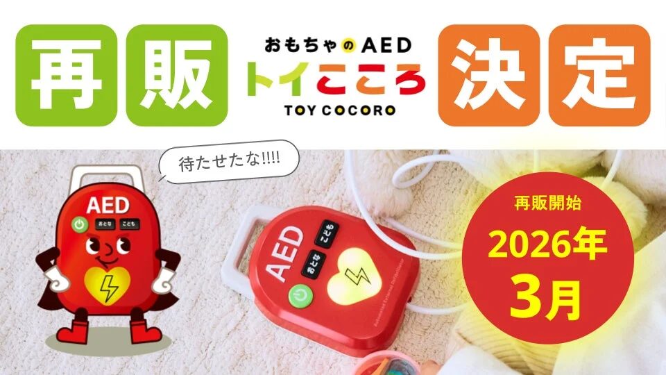 「おもちゃのAED トイこころ」の再販が2026年3月に決定したことを告知する画像です。AEDのキャラクターと実物の玩具が描かれ、「待たせたな!!!!」というメッセージと共に再販開始日を伝えています。