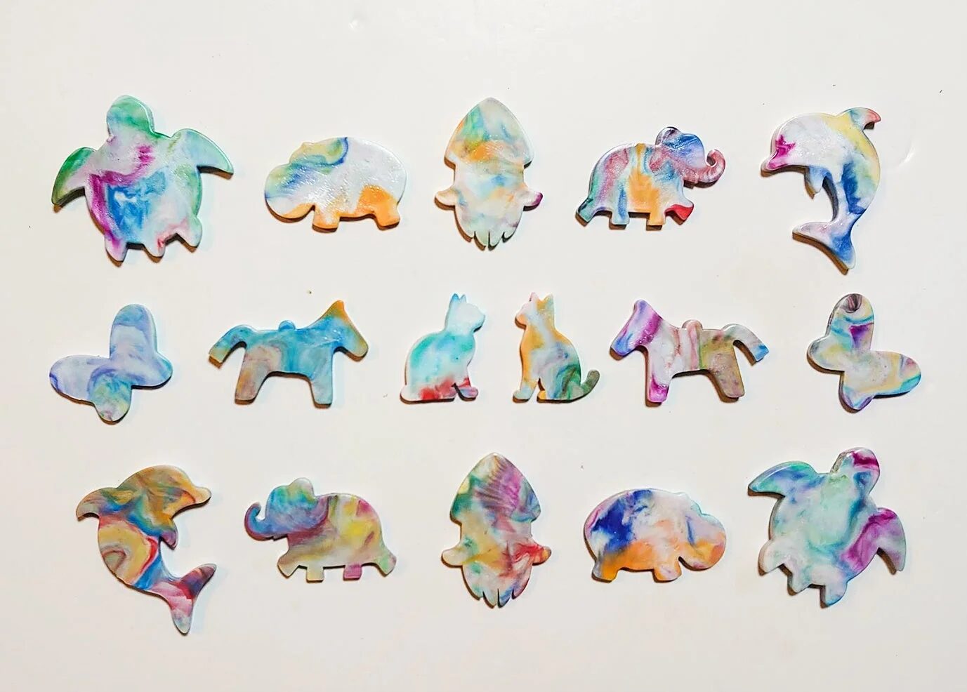 様々な動物の形をした、カラフルなマーブル模様のクラフト作品が白背景に並べられています。