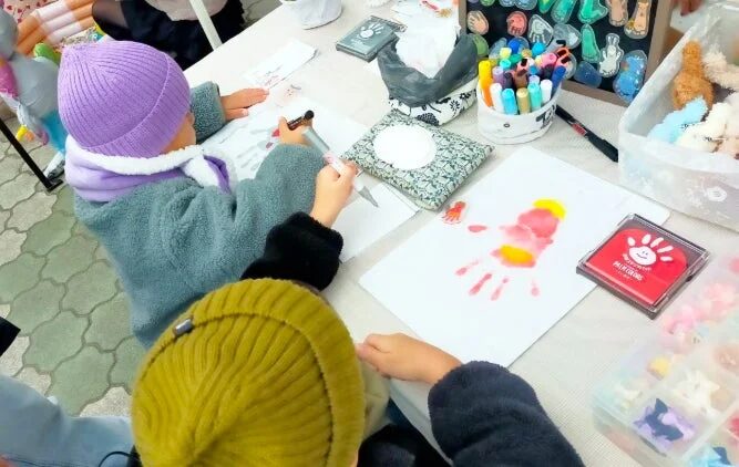 子供たちがテーブルで手形アートや絵を描くクリエイティブな活動に集中している様子