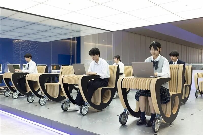 現代的な学習空間で、複数の学生が車輪付きのユニークな木製デスクチェアに座り、ノートパソコンを使って学習している様子