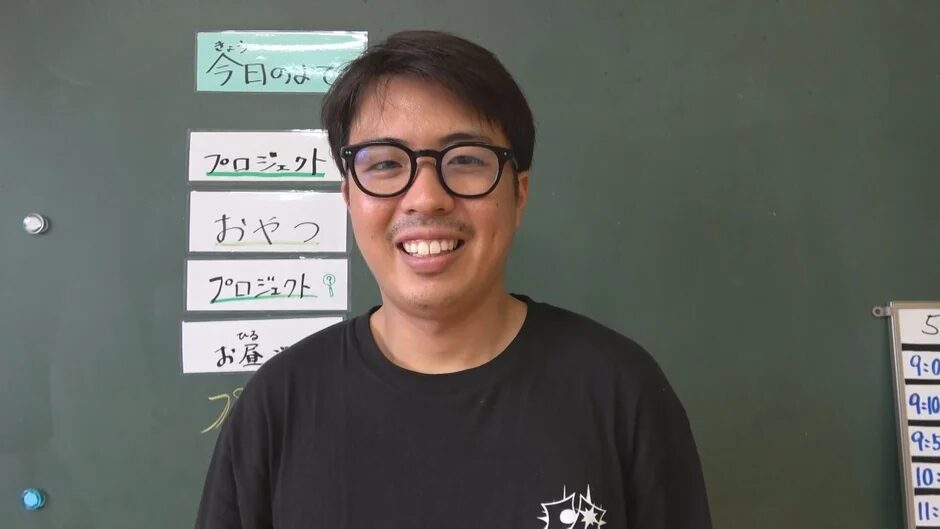 笑顔で黒板の前に立つ男性