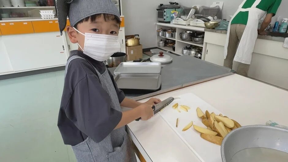 コック帽とエプロンを着用し、じゃがいもを切る子供