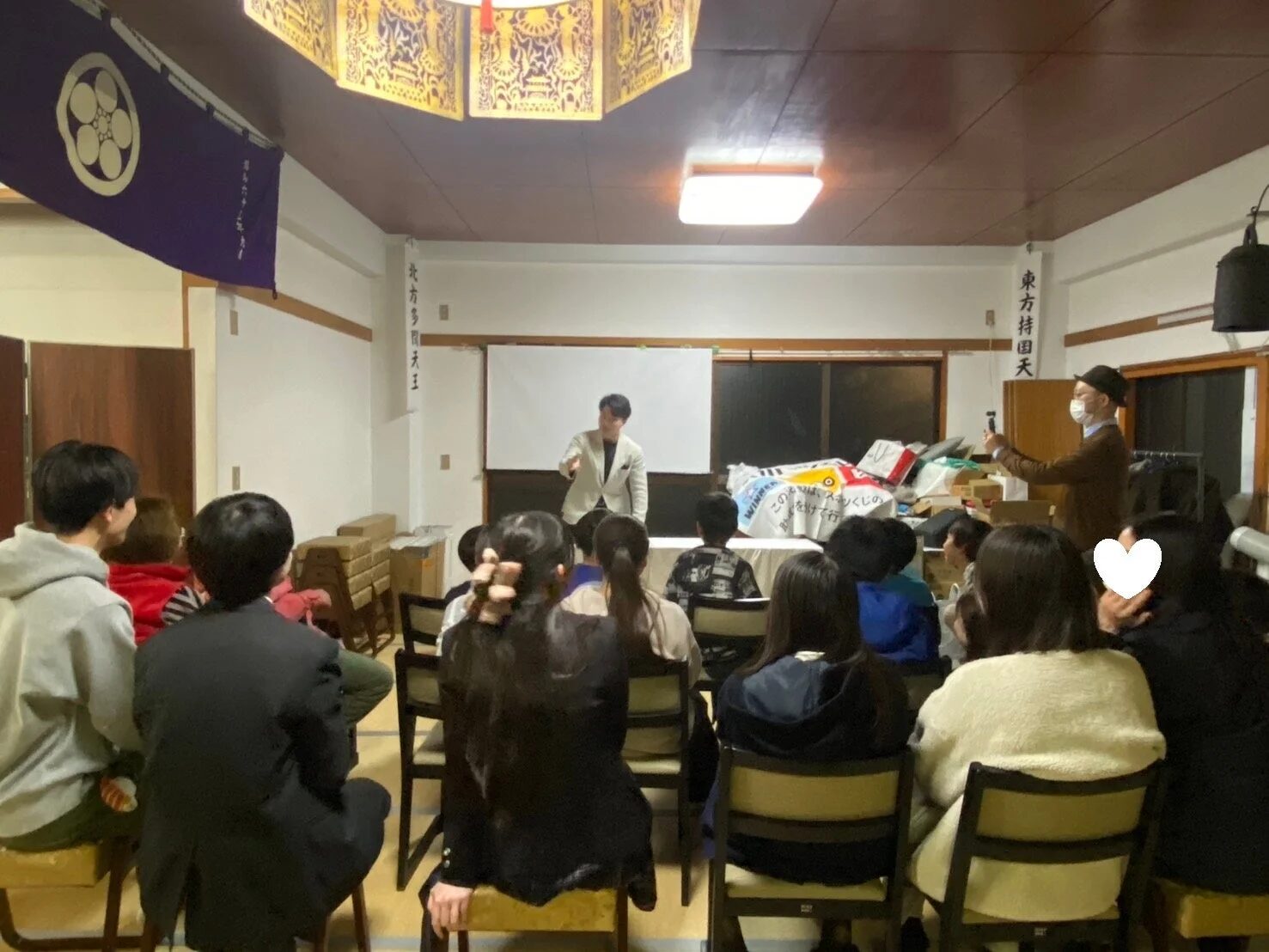 和室のような空間で多くの聴衆が座っている様子