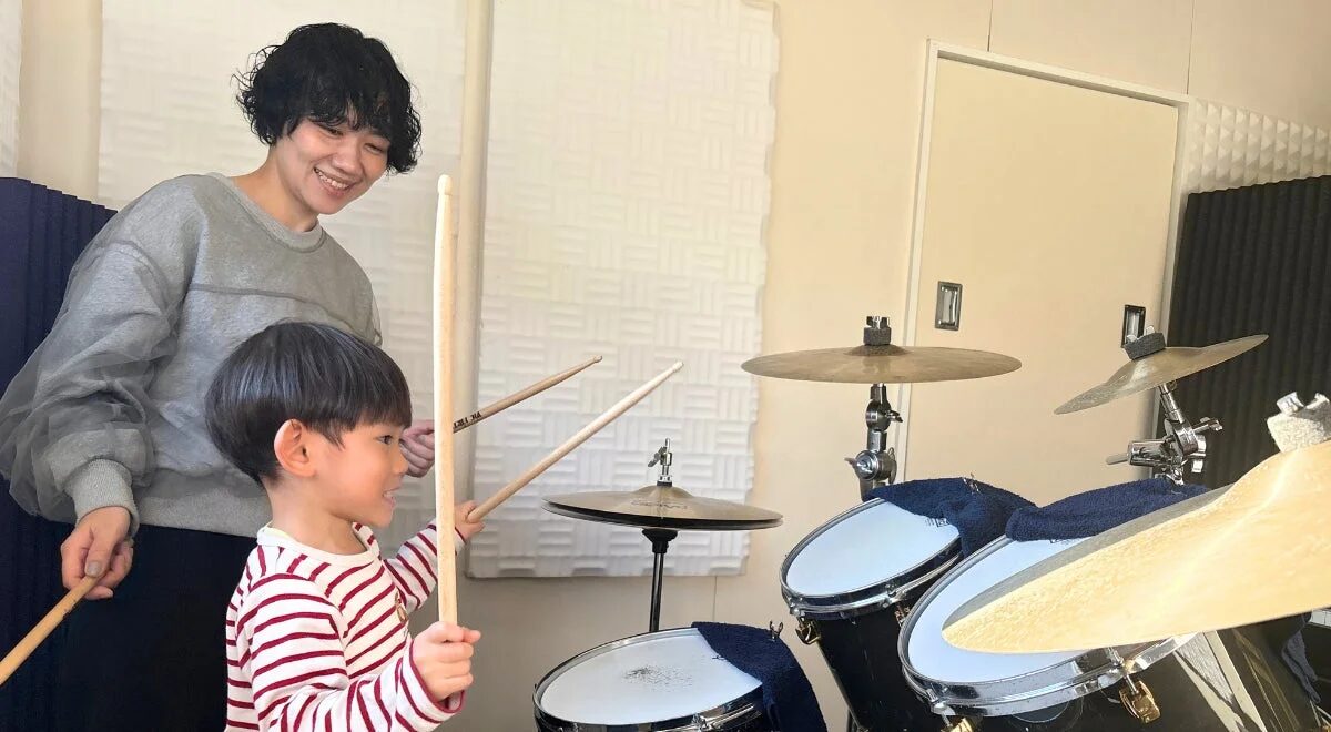 ドラムセットのある音楽室で、女性が子供にドラムを教えている様子
