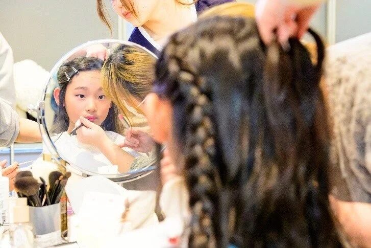 若い女の子が鏡を見ながらプロのメイクアップアーティストにメイクを施してもらっています