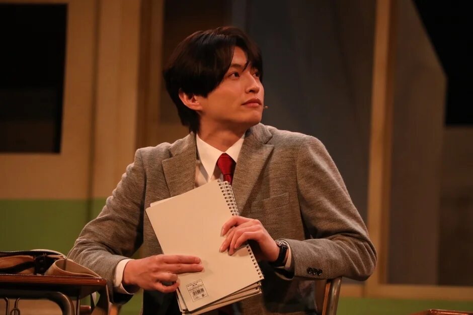 スーツ姿でノートを抱える教師役の男性