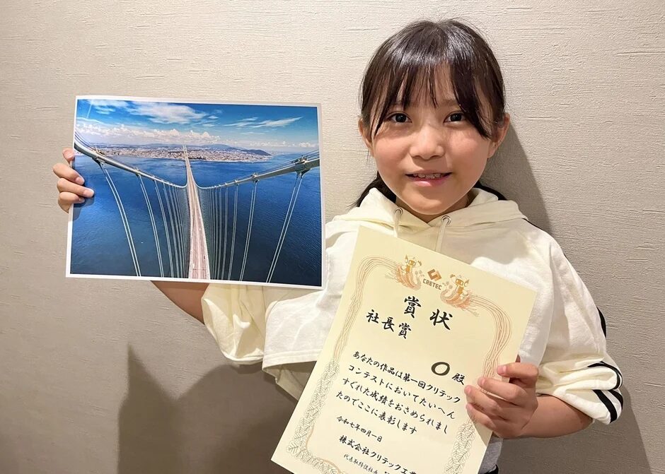 社長賞の賞状と橋の写真を持つ少女