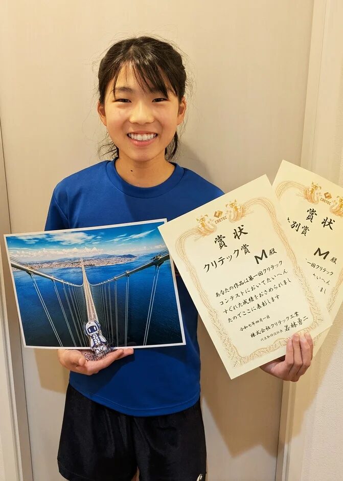 賞状を持つ笑顔の少女と橋の写真