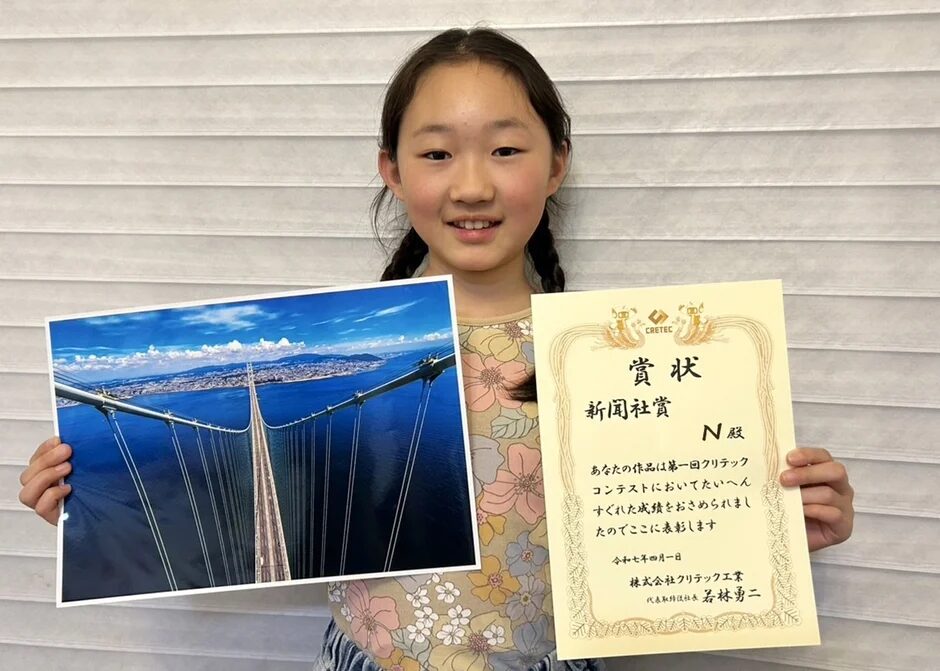 新聞社賞の賞状と吊り橋の写真を持つ少女