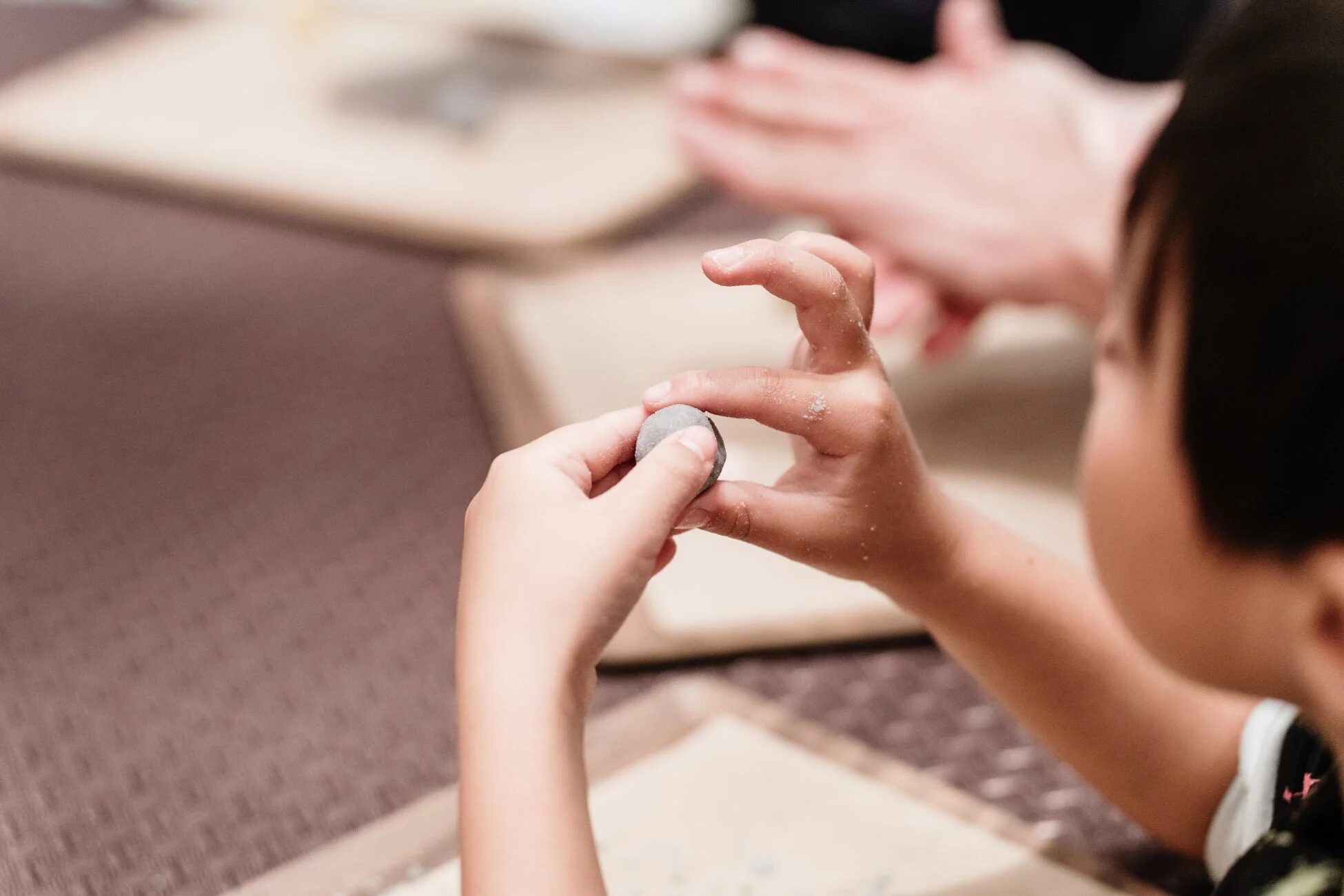 子供が両手で小さな粘土のようなものを丸めている様子