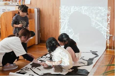 子供と大人が床に広げた紙にアート活動をする様子